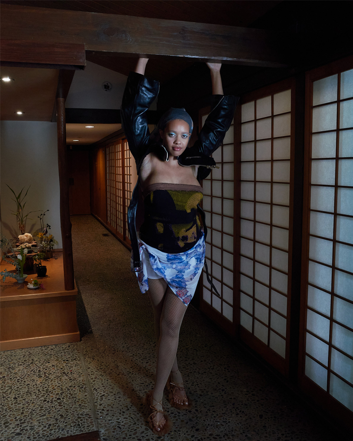 Female model standing with hands outstretched towards a ceiling beam in a traditional japanese house looking toward the camera